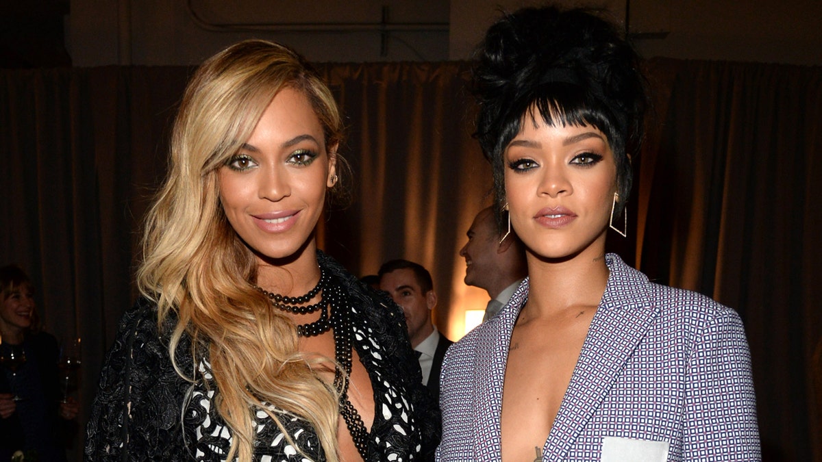 Beyonce wearing a black and white outfit while standing next to Rihanna wearing a blazer
