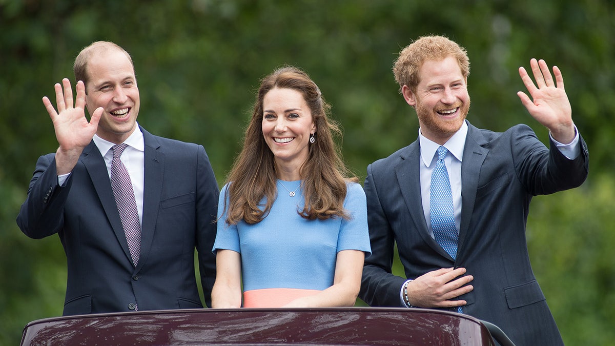 Prince William, Kate Middleton and Prince Harry standing next to each other smiling and waving to the crowd.