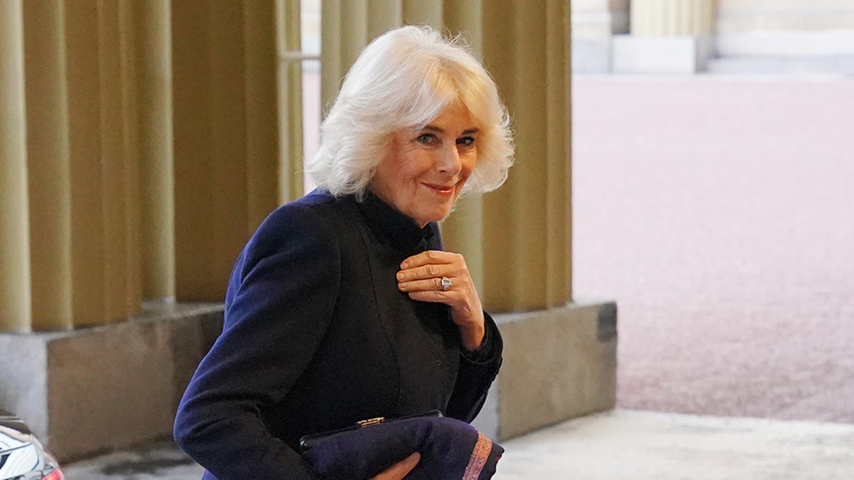 Queen Camilla holding onto her coat and smiling