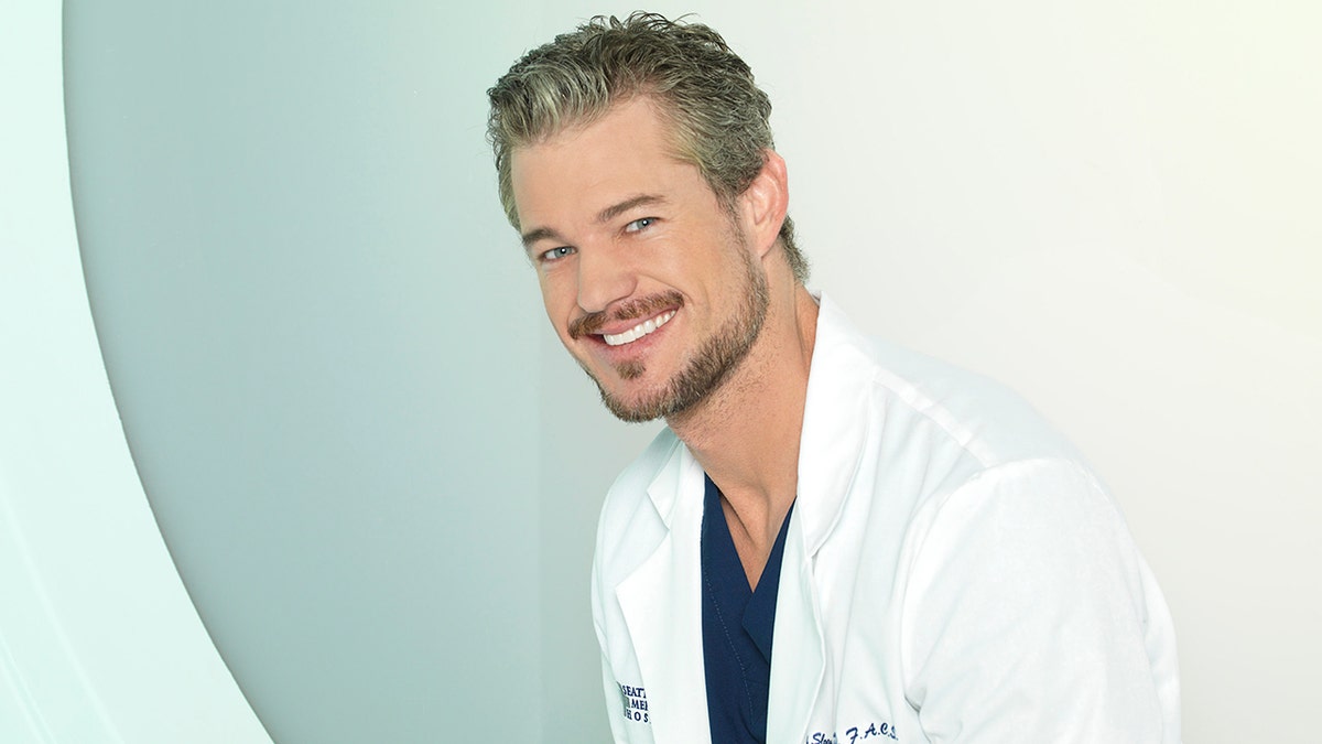 Eric Dane as Dr. Mark Sloan on "Grey's Anatomy" wearing a white coat and dark blue scrubs