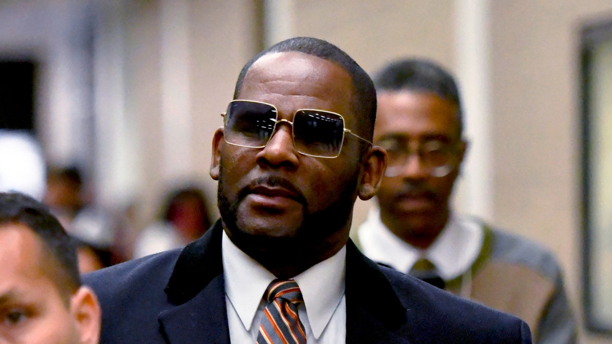R Kelly wears a blue coat and red tie outside of court