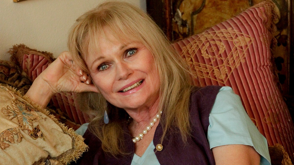 Valerie Perrine smiles at home on her couch