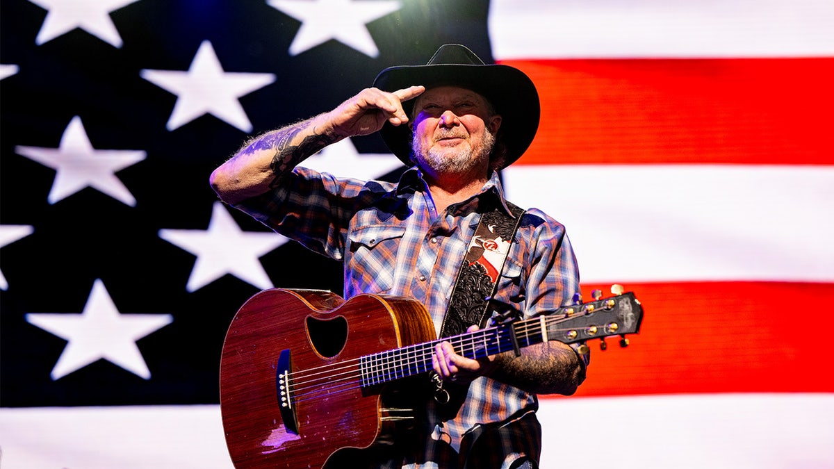 Tracy Lawrence holds guitar in front of flag