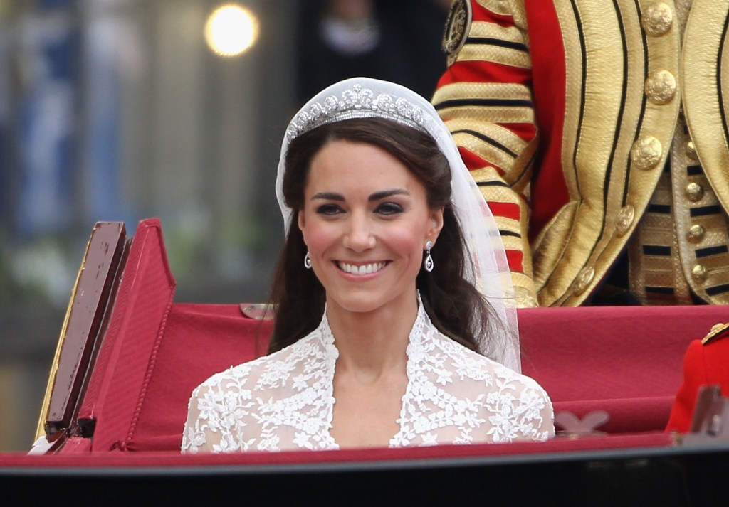 Catherine, Duchess of Cambridge, smiling in her wedding gown and veil, riding in a carriage.