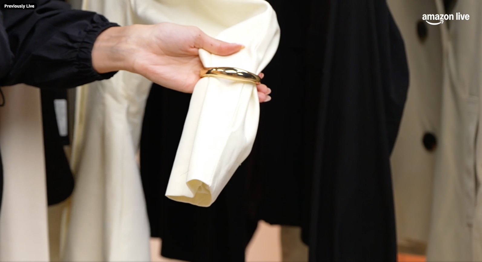 A hand holding a white sleeve gathered by a gold bracelet.