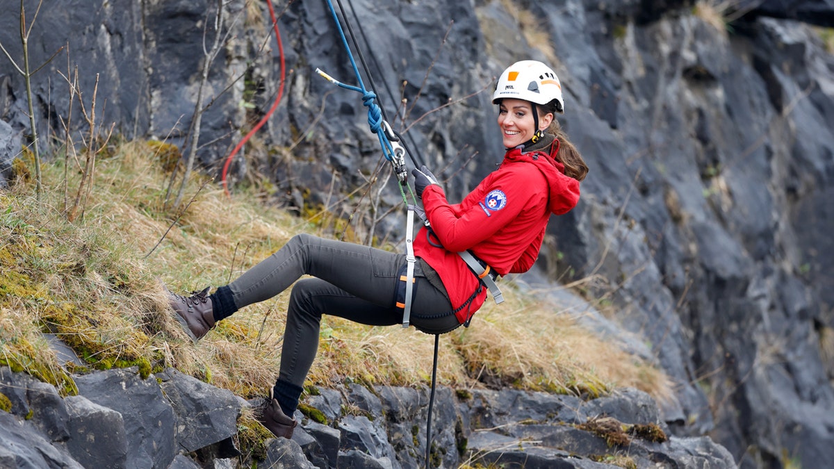 Kate Middleton wears a helmet and red jacket while rock climbing