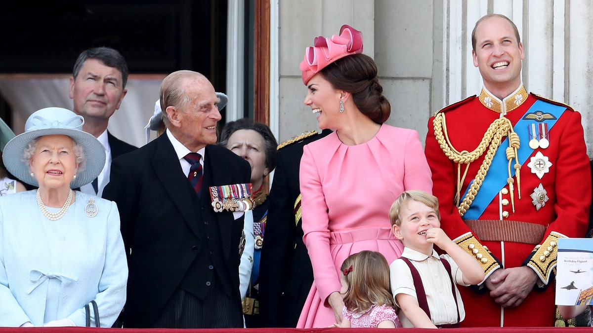 Queen Elizabeth II, Prince Philip, Catherine, Princess Charlotte, Prince George, and Prince William standing on a balcony.