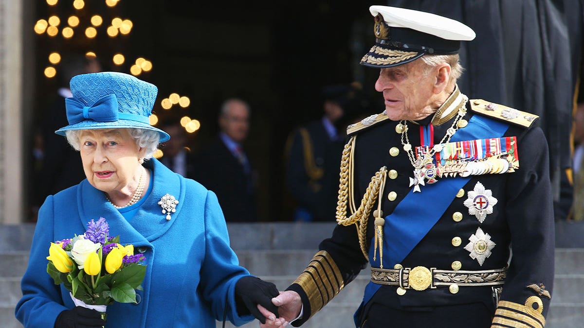 Prince Philip holding Queen Elizabeth's hand during a royal engagement.