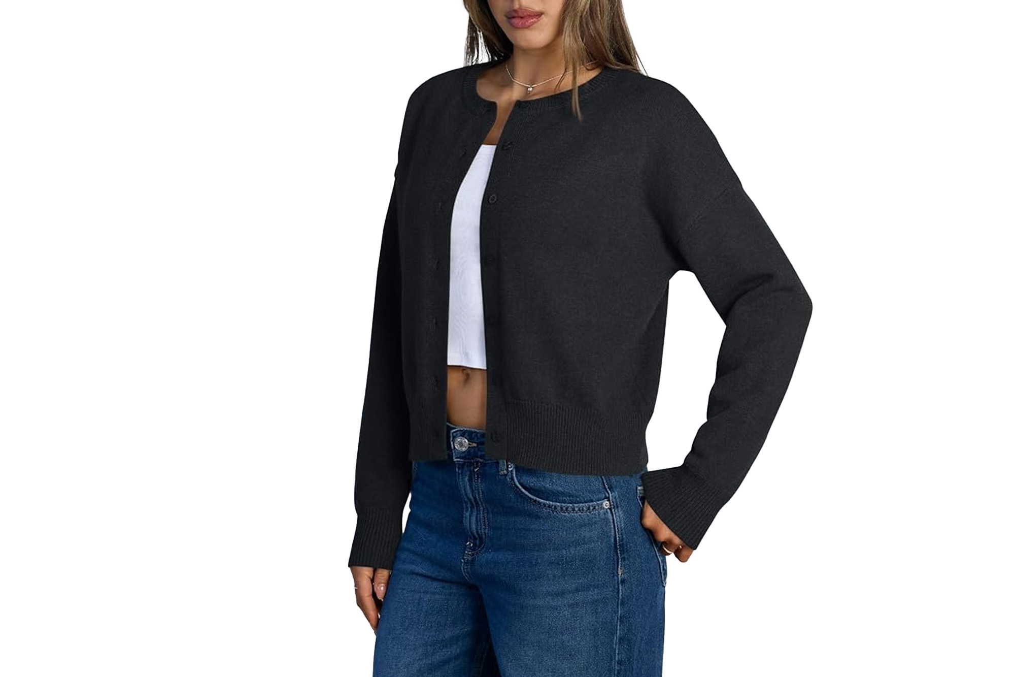 Woman wearing a black button-up cardigan over a white crop top and blue jeans.