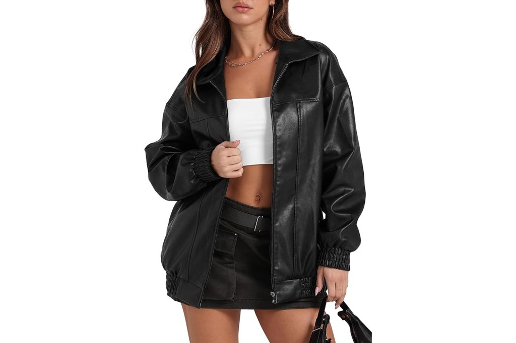 A woman models an open black oversized faux leather jacket over a white crop top and black mini skirt.