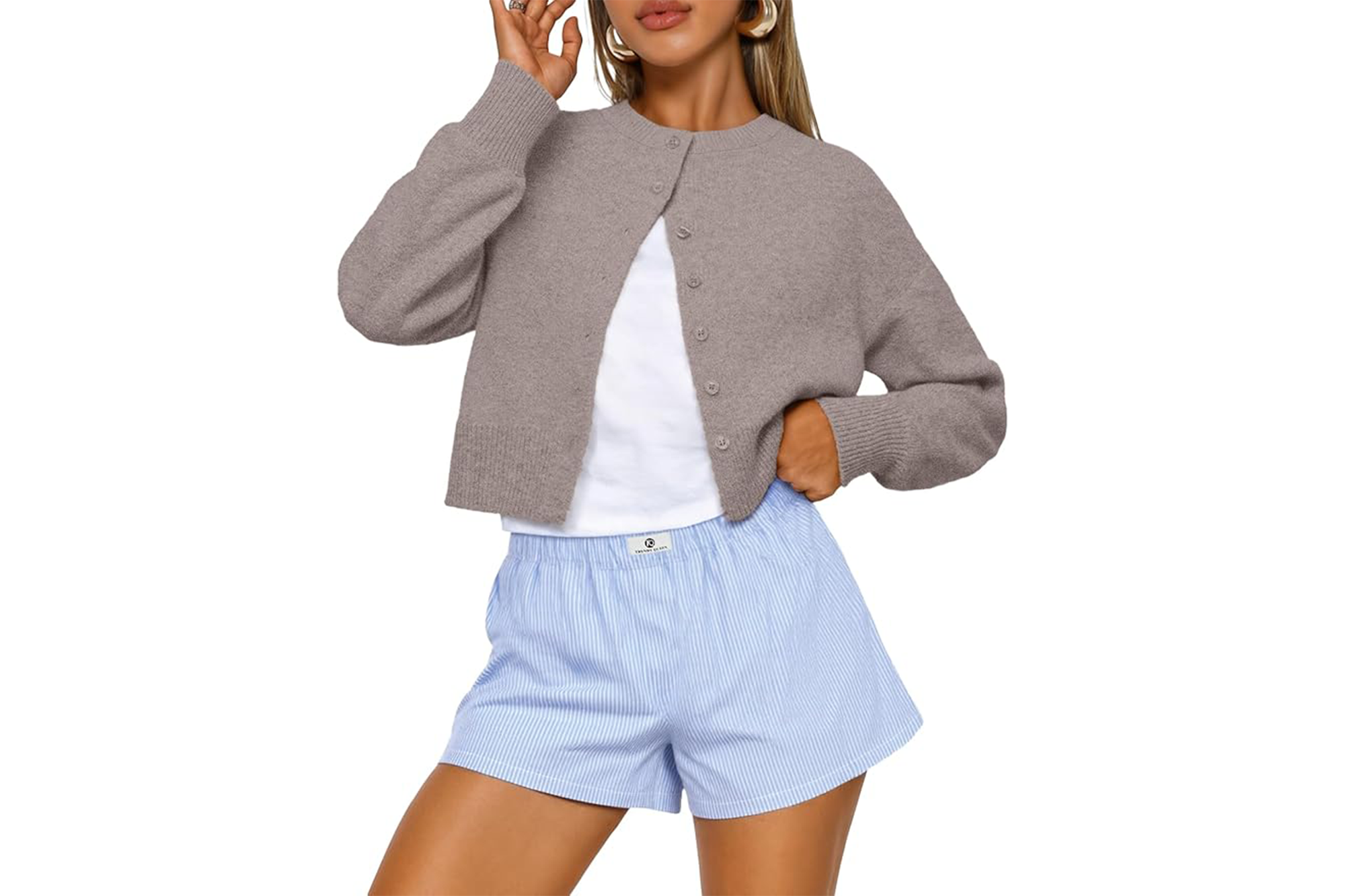 A woman wearing a cropped grey cardigan, a white t-shirt, and blue and white striped shorts.