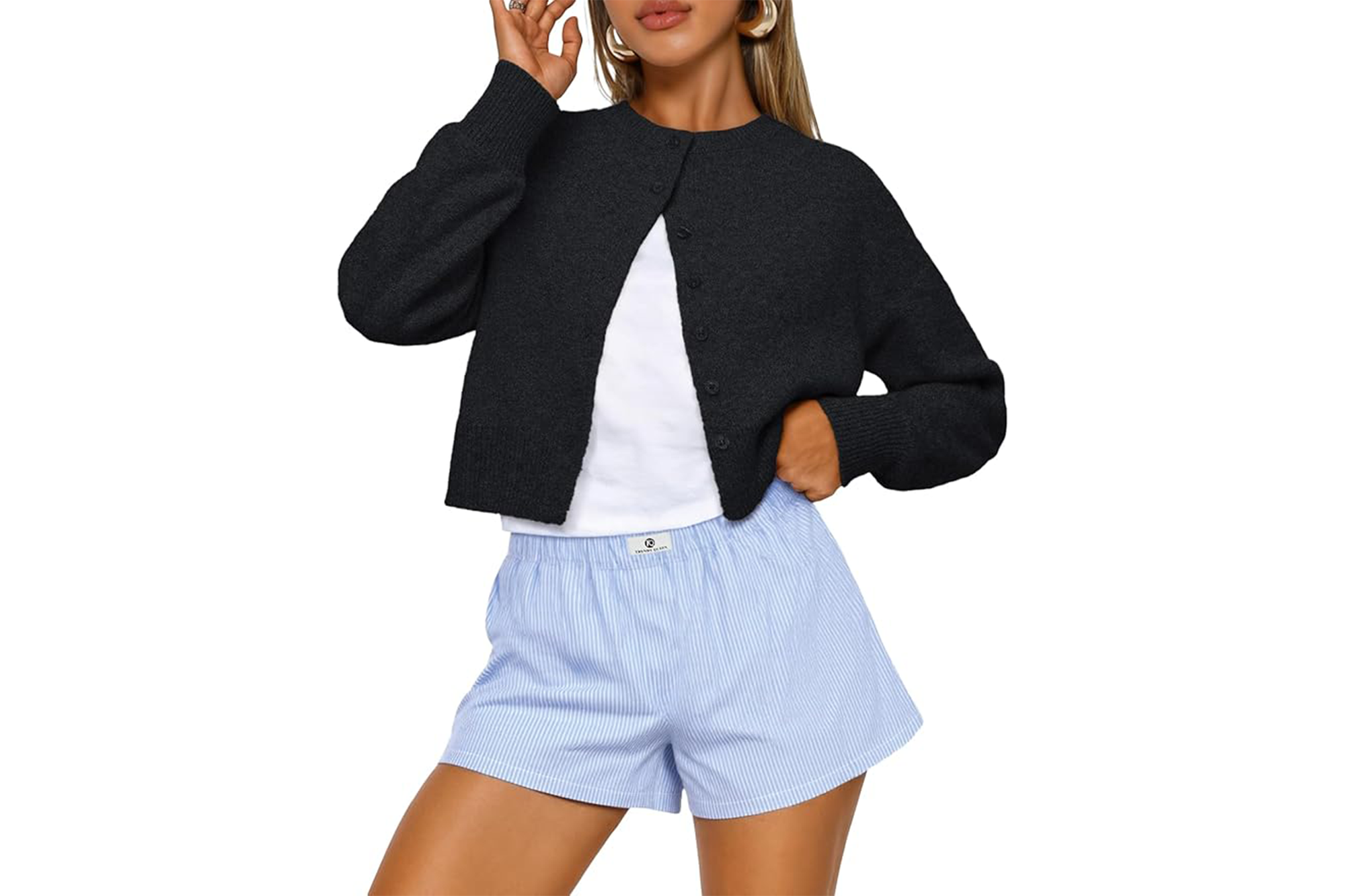 A woman wearing a cropped black cardigan, a white t-shirt, and blue and white striped shorts.