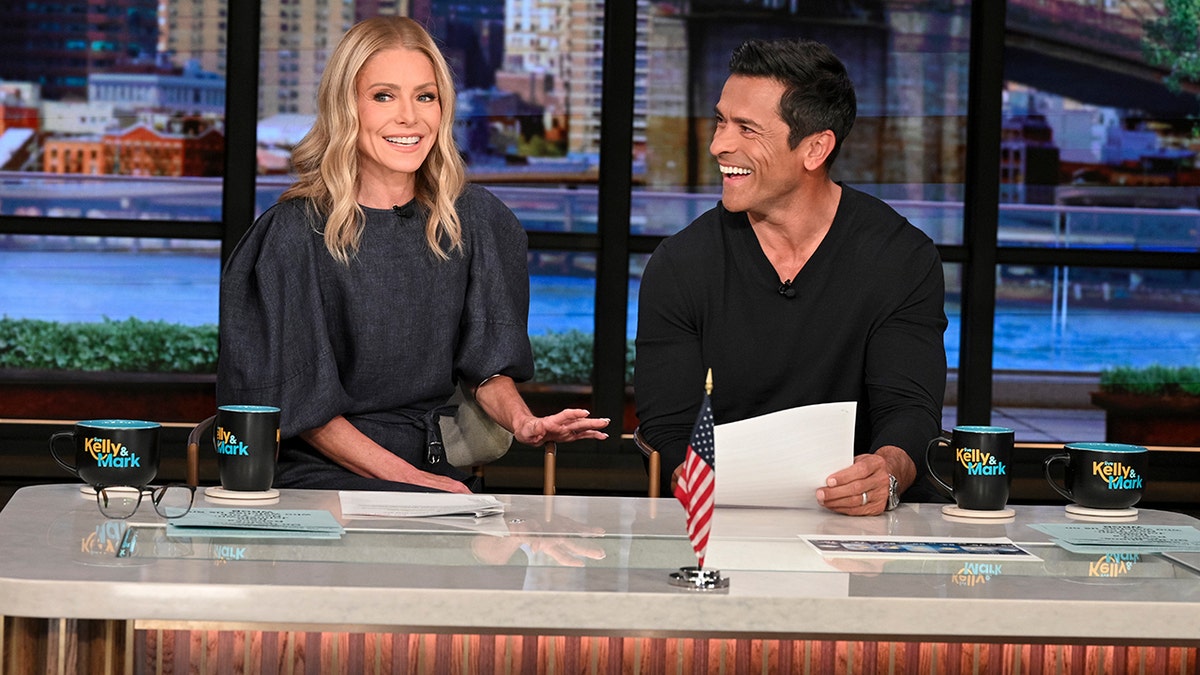 Kelly Ripa and Mark Consuelos behind the desk while hosting "Live with Kelly and Michael" in June 2025.