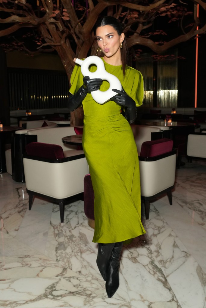 Kendall Jenner in a lime green dress and black gloves holding a white 818 Tequila bottle.