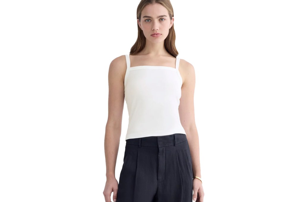 A woman wearing a white square-neck tank top and dark trousers.