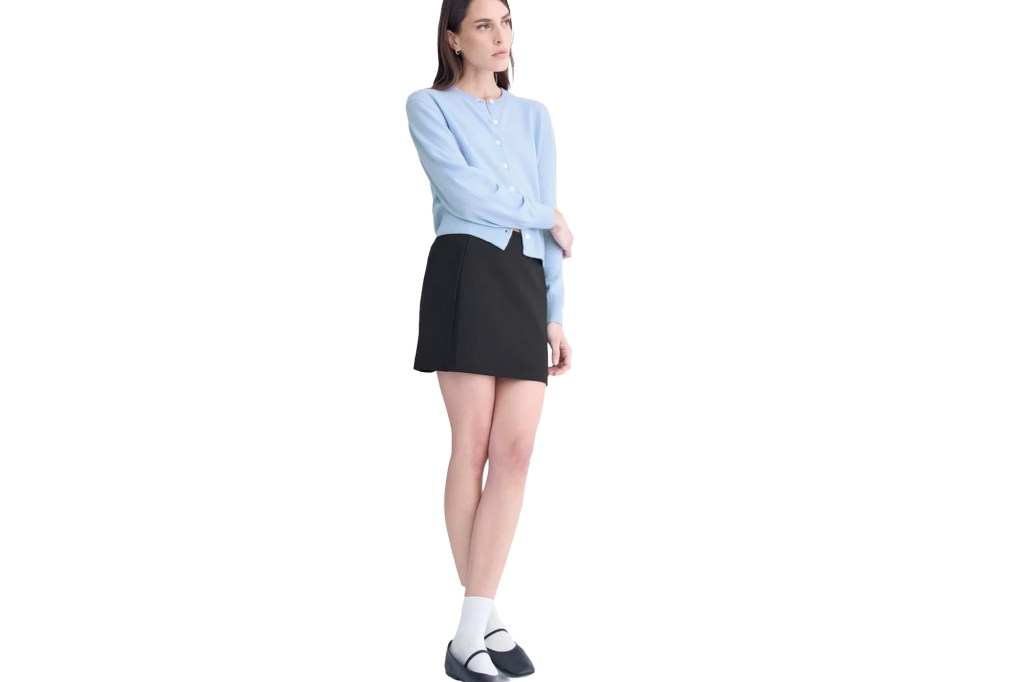 Woman wearing a light blue cardigan and a black mini skirt.