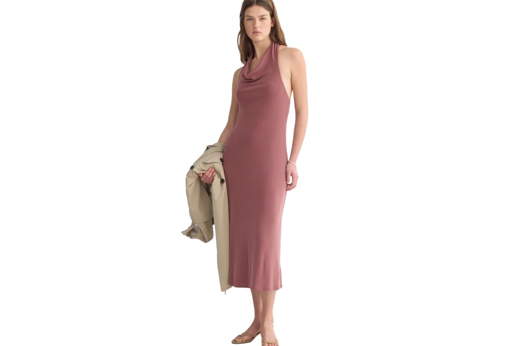 A woman in a dusty rose halter neck dress holding a beige jacket.