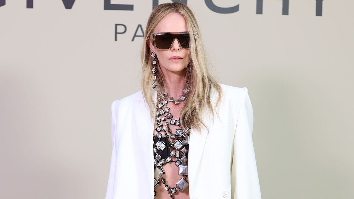 Charlize Theron in a white suit and chain details at the Givenchy fashion show in October 2025.