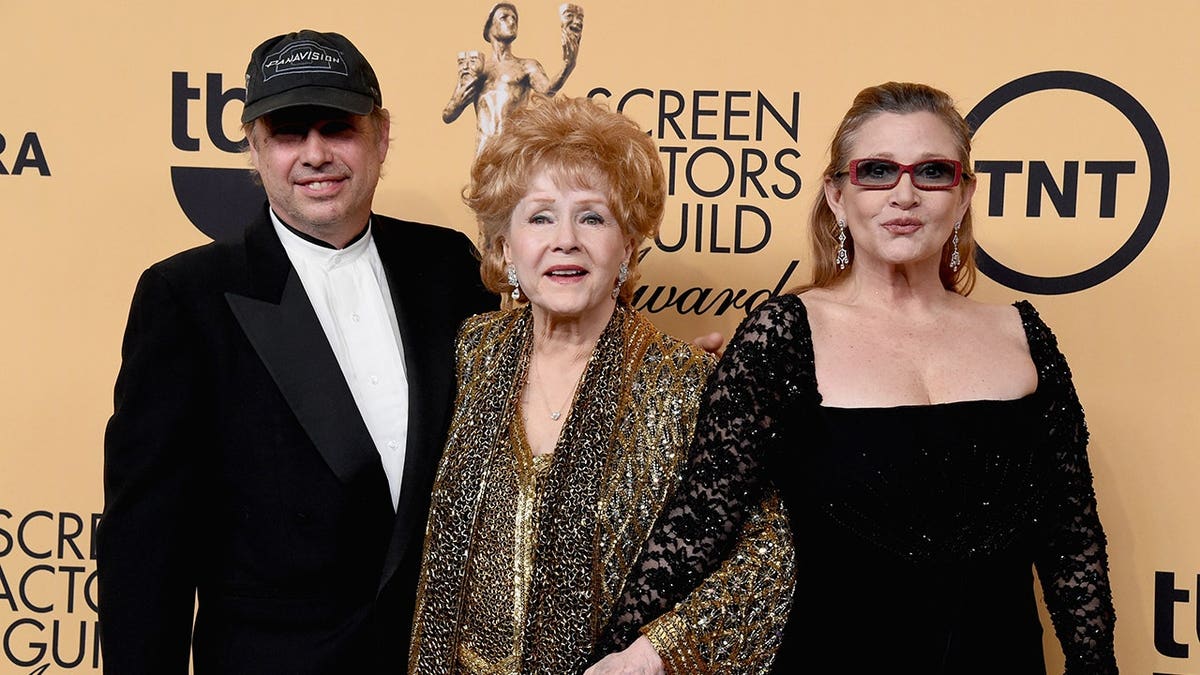Todd Fisher, Debbie Reynolds, and Carrie Fisher posing in a press room.