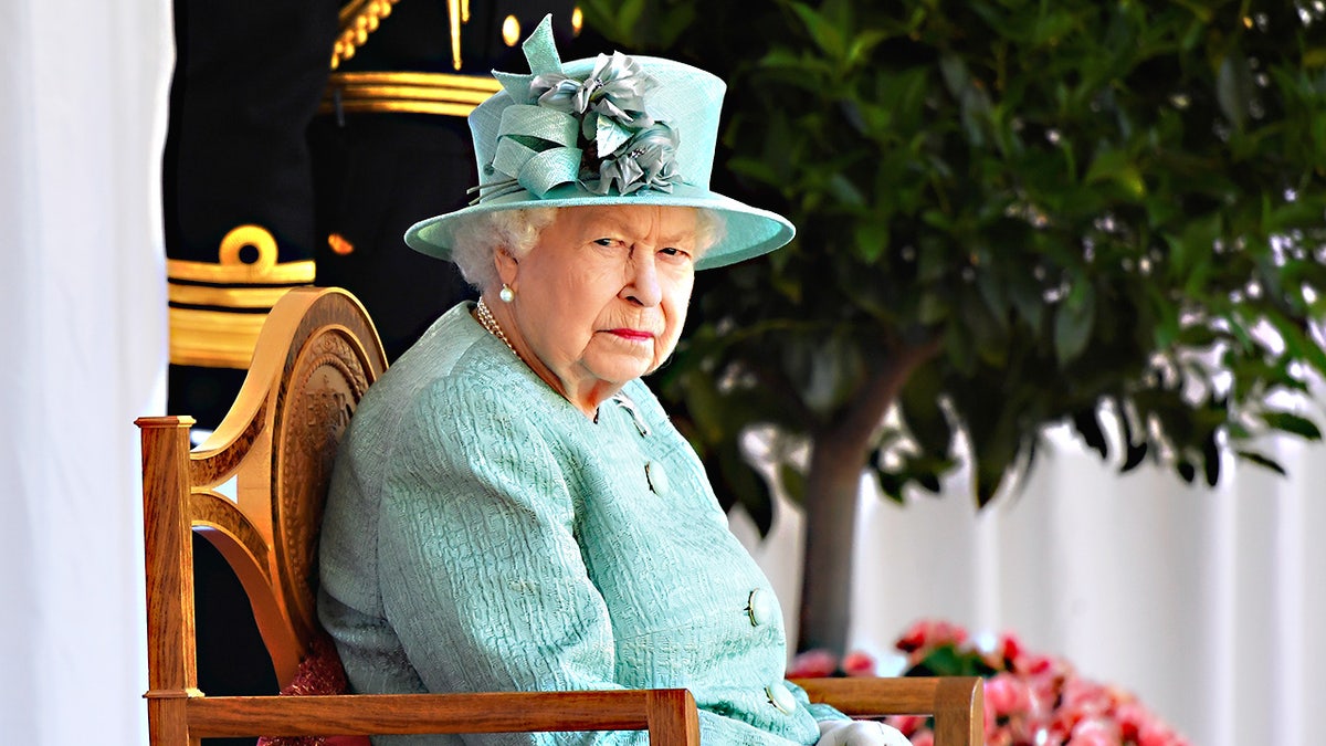 Queen Elizabeth II sitting on a chair wearing a light blue coat dress and matching hat in Windsor
