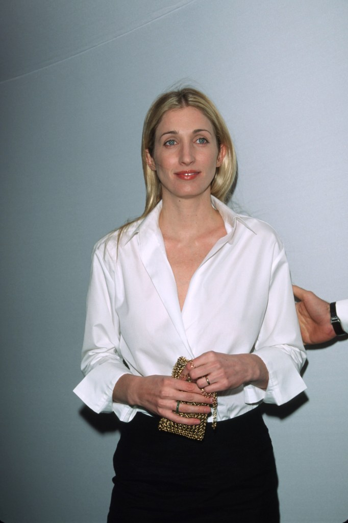 Carolyn Bessette Kennedy in a white shirt, holding a gold purse.