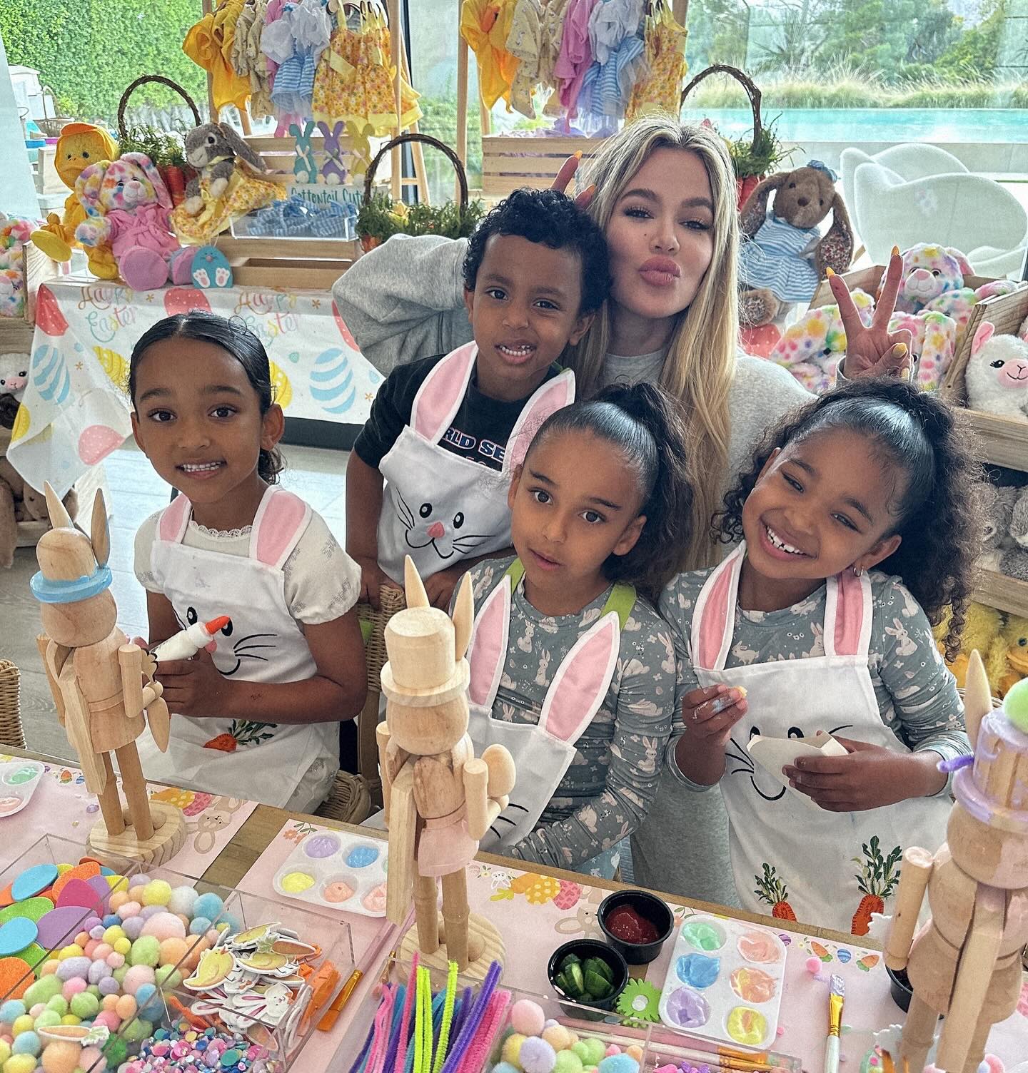 Khloé Kardashian with four children in bunny aprons, celebrating Easter.