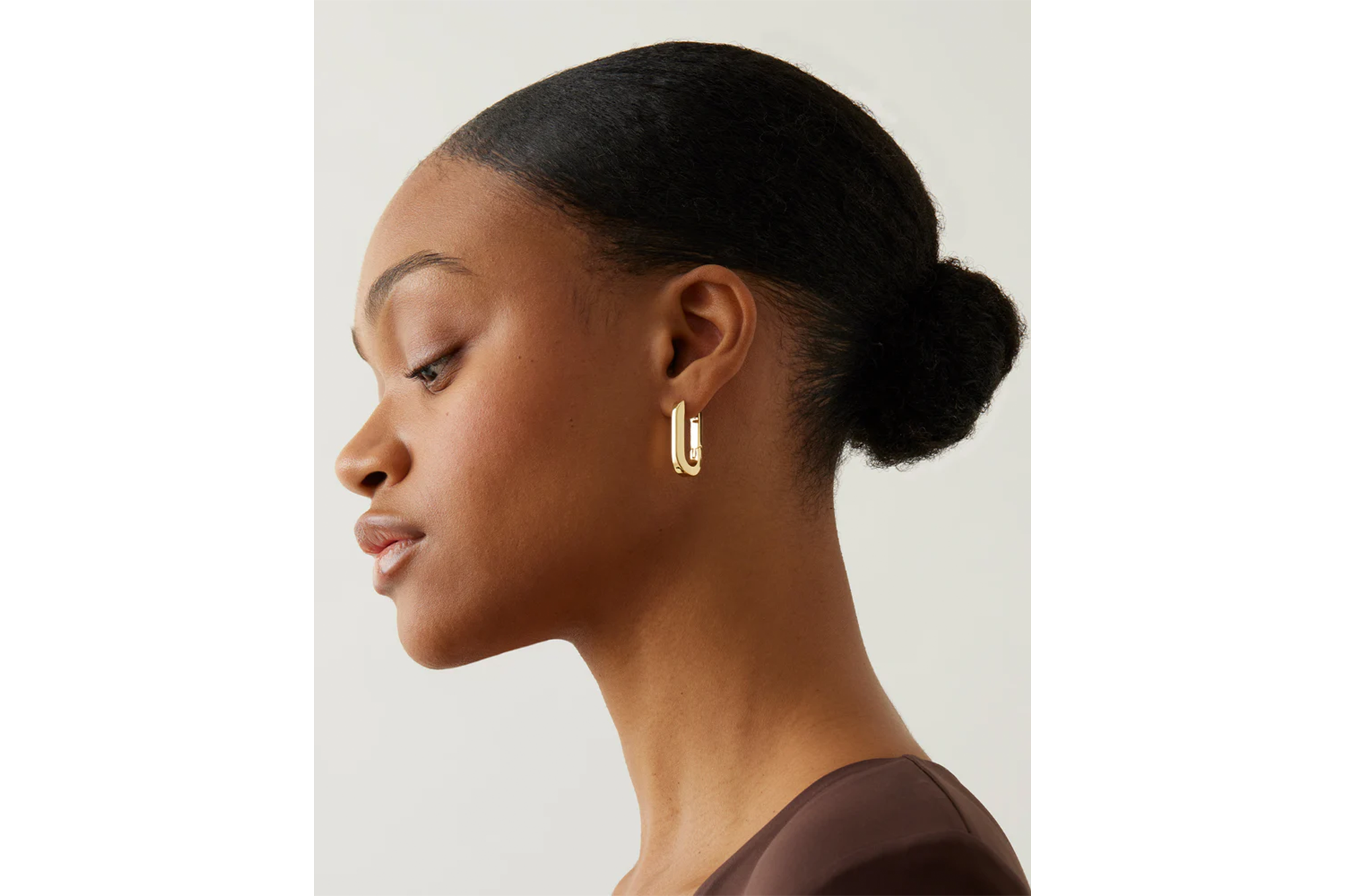 A woman with dark hair in a bun wears a single gold U-shaped hoop earring.