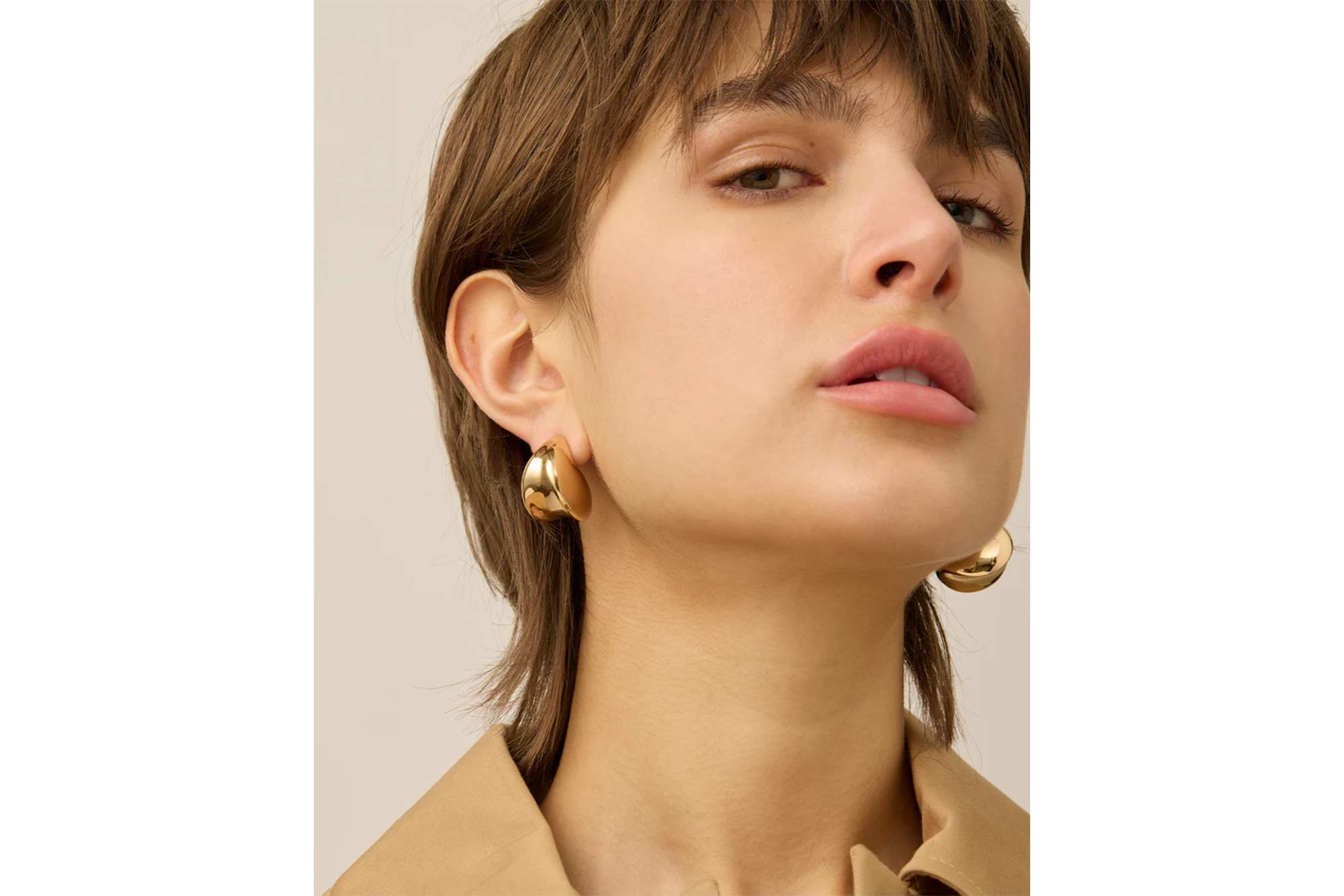 A woman wearing gold dome earrings.