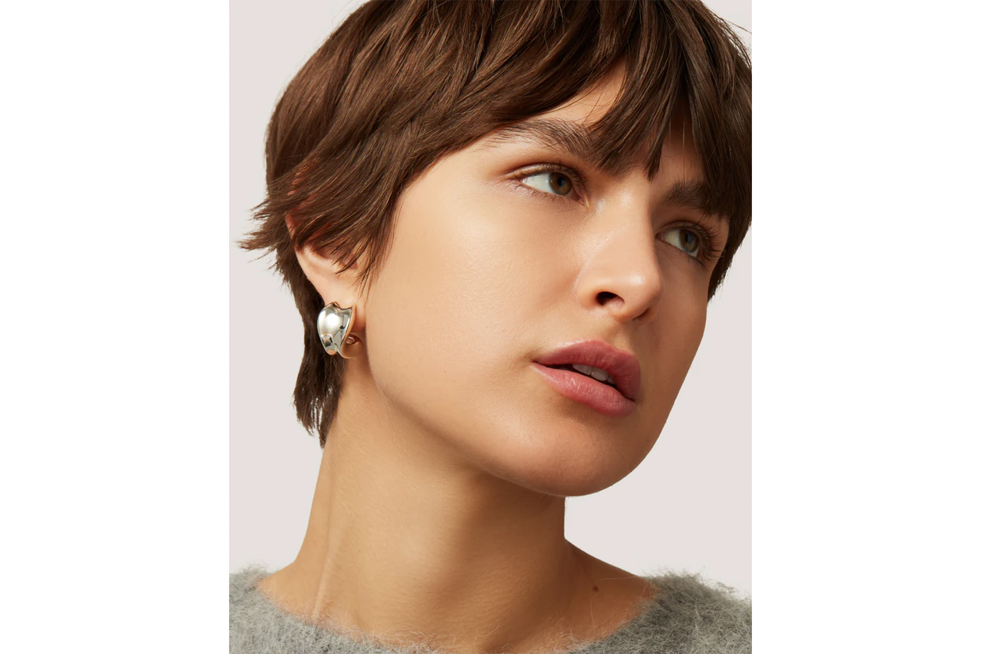 Woman with short brown hair modeling a silver heart-shaped earring.