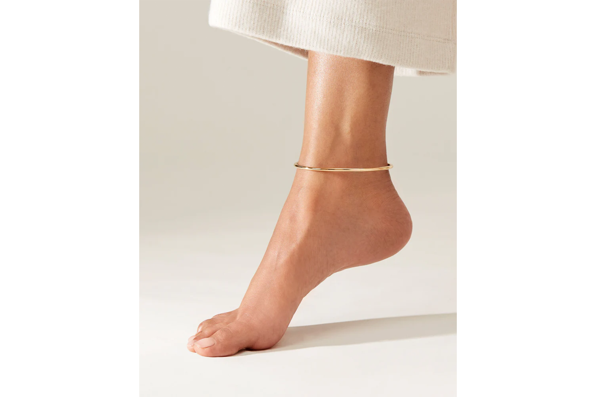 A rose gold anklet on a model's left ankle.