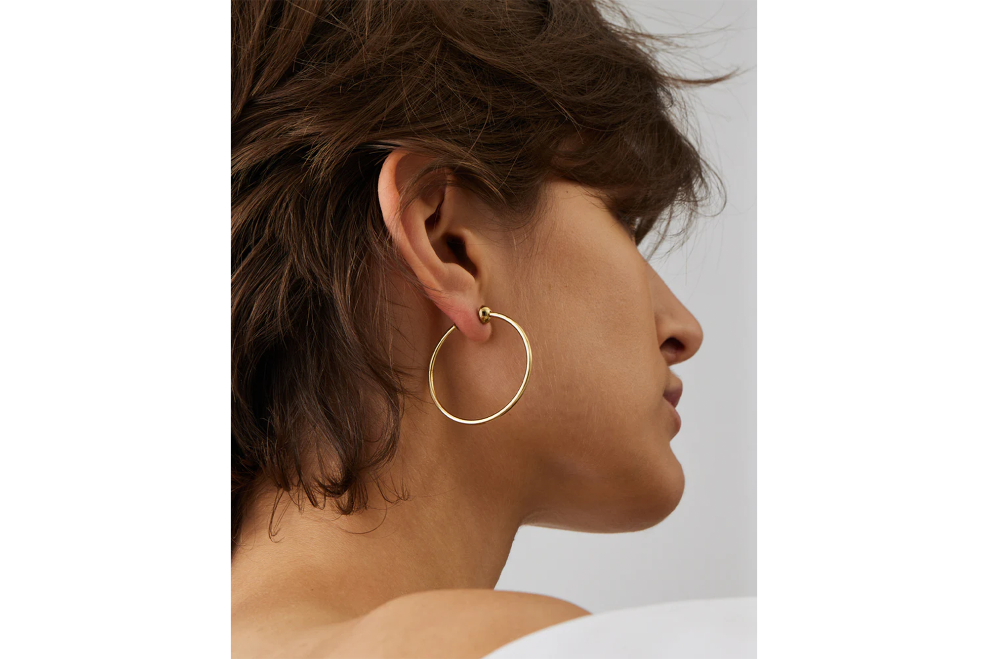 Side view of a person wearing a single gold hoop earring.
