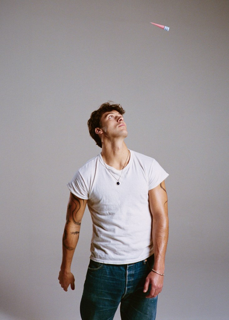 A man in a white t-shirt looking up at a pink dart in mid-air.