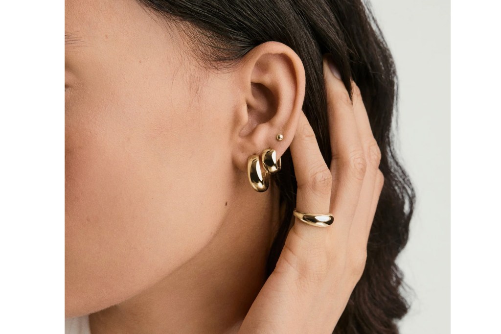 A person wearing a golden ring and golden hoop earrings, with dark hair cascading over the ear.