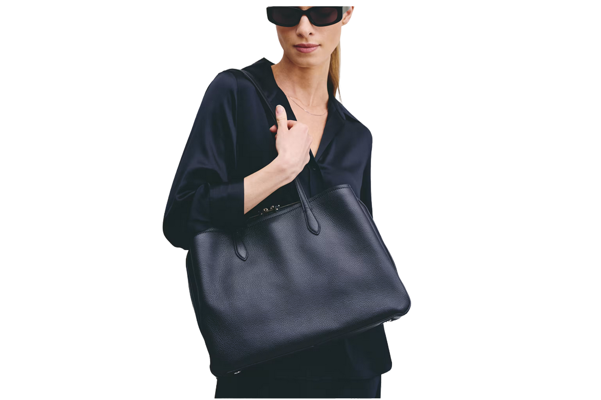 A woman wearing sunglasses and a black blouse carries a black leather tote bag.