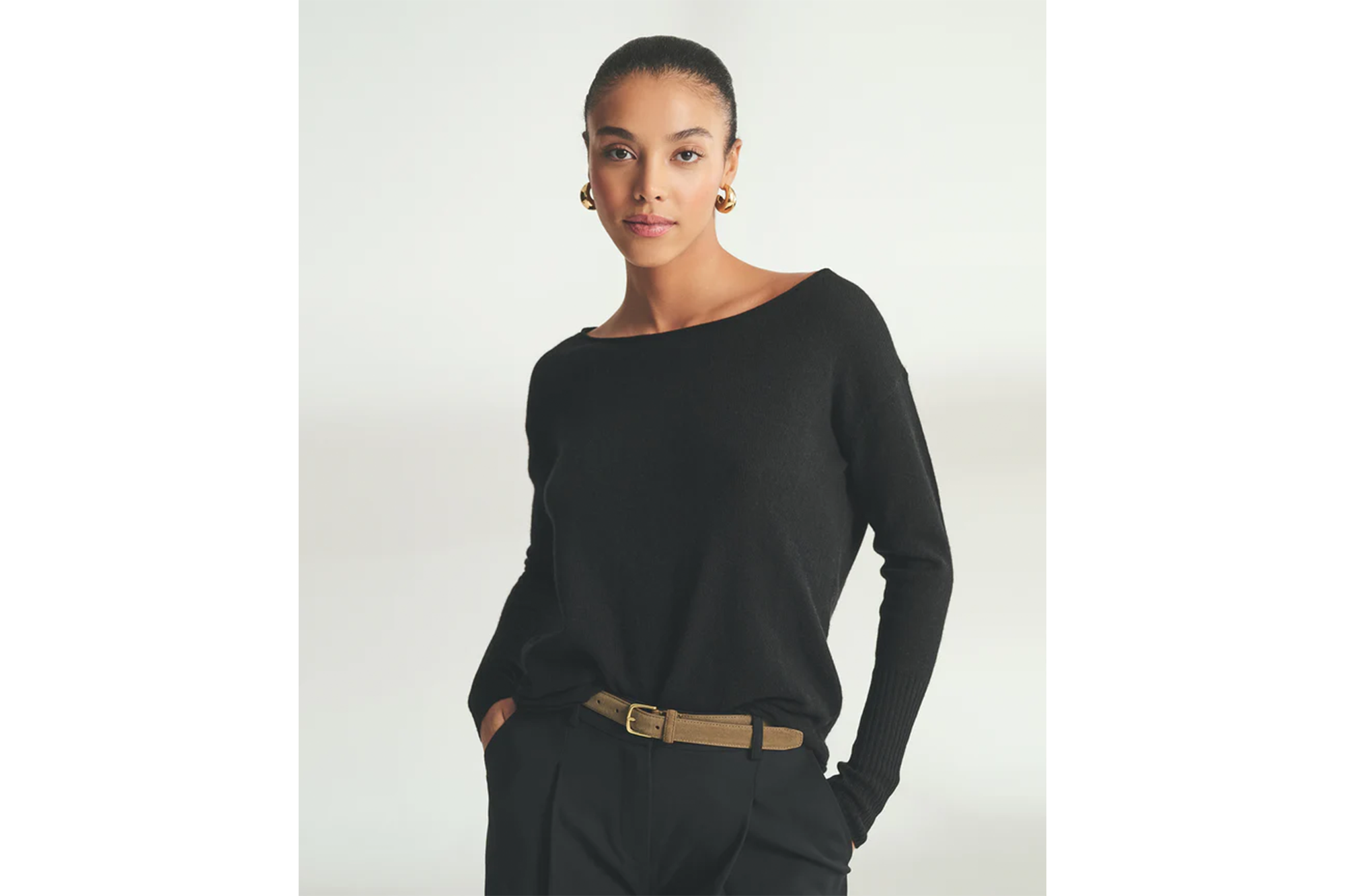 Model in black boatneck sweater, black trousers, and a khaki belt.