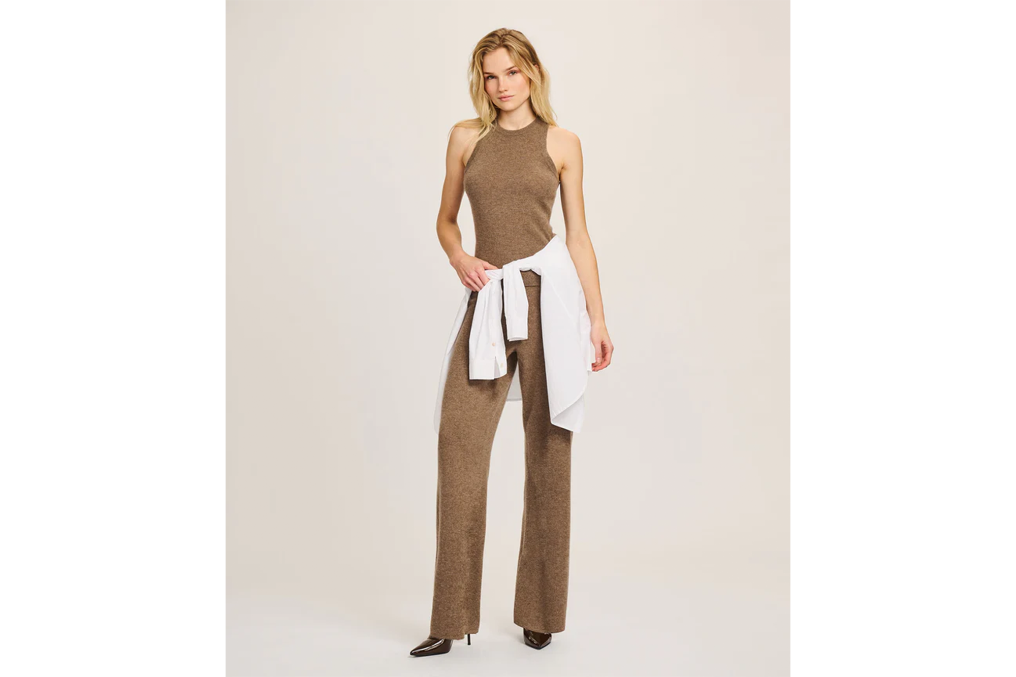 Woman wearing a brown ribbed tank top and matching wide-leg pants, with a white button-down shirt tied around her waist.