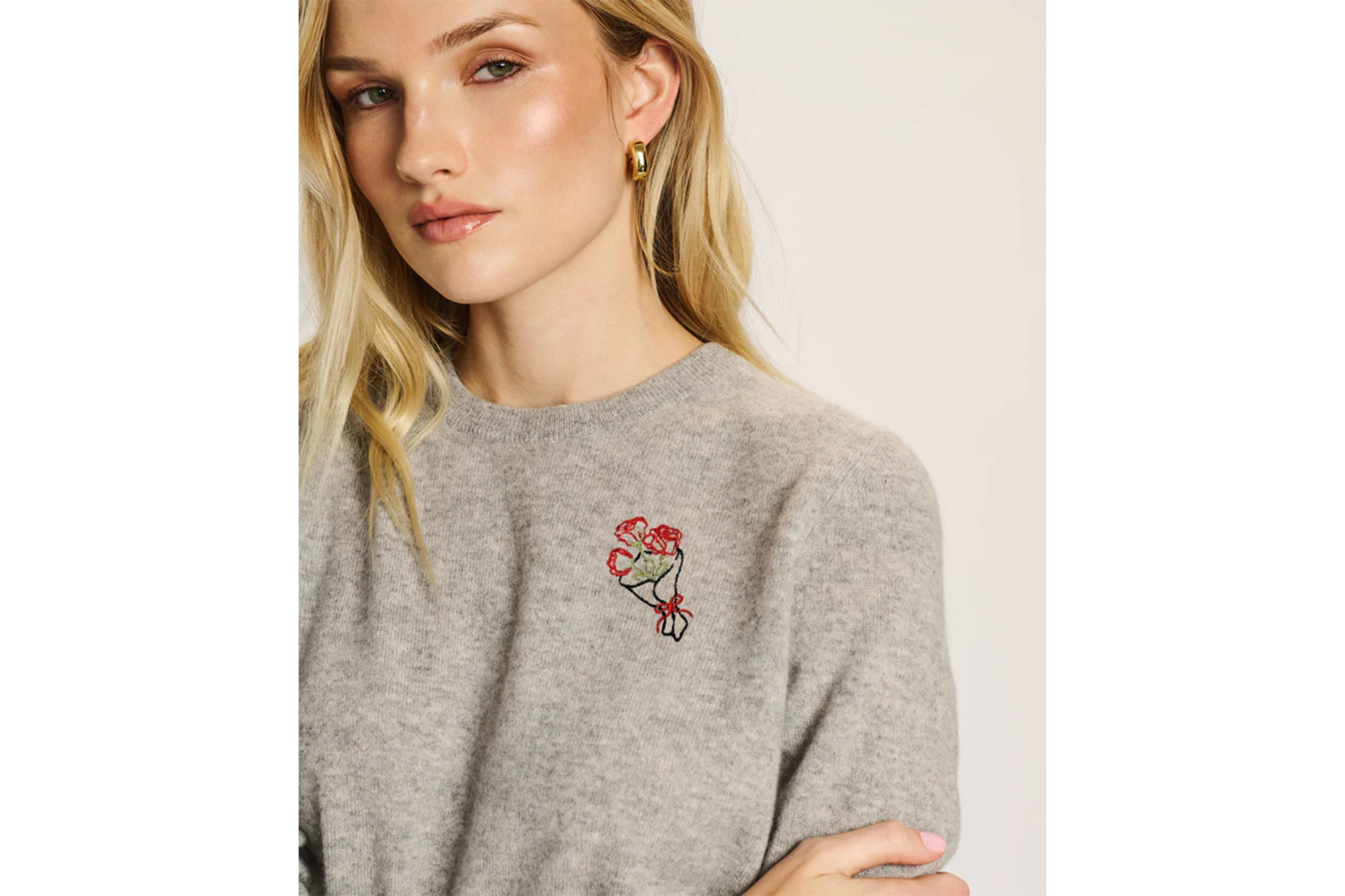 Woman wearing a grey sweater with a bouquet of flowers embroidered on it.