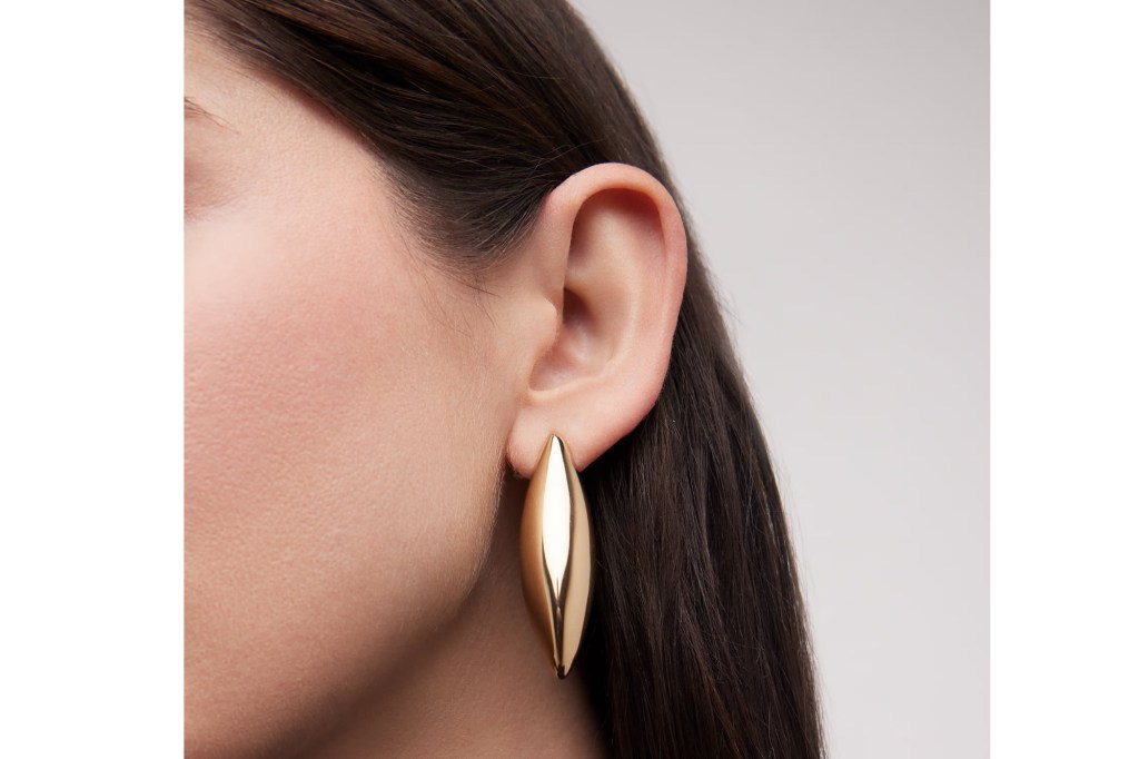 A close-up of a person wearing a large, gold, dagger-shaped earring.