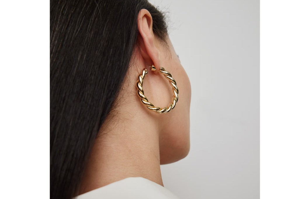 Close-up of a person wearing a gold twisted hoop earring.