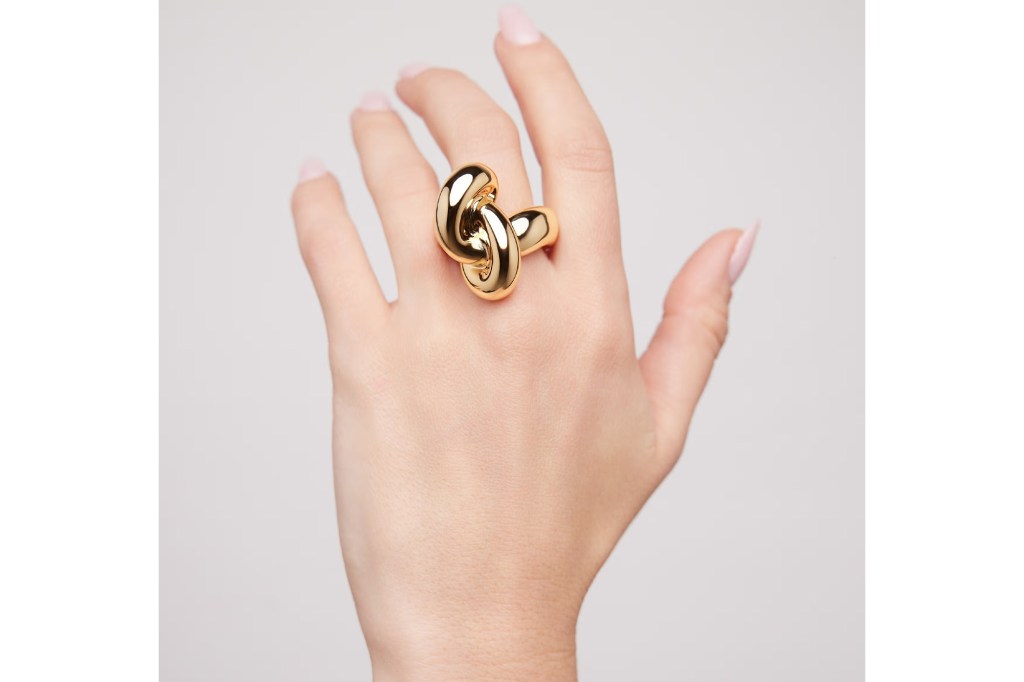 A person's hand wearing a large, shiny gold ring shaped like a knot.
