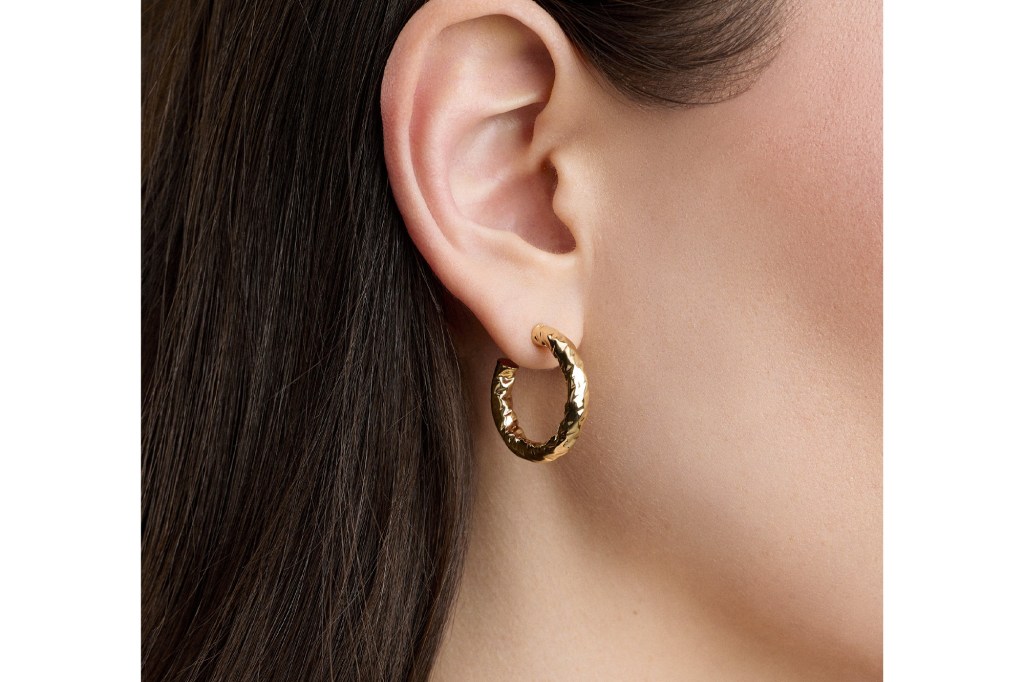 Close-up of a Hailey hammered gold hoop earring on an ear.
