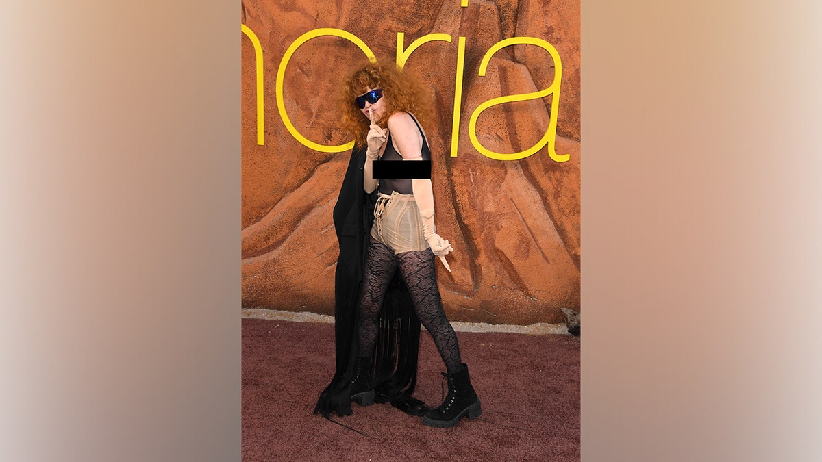 Natasha lyonne poses with her finger over her lips.