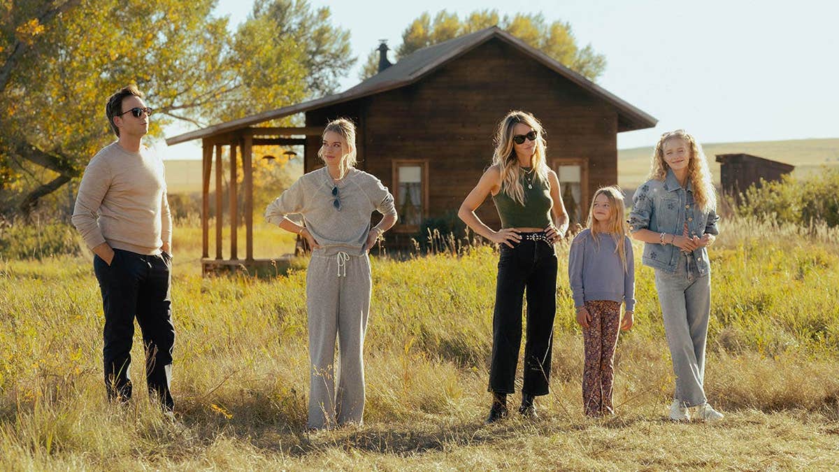 Patrick J. Adams, Elle Chapman, Beau Garrett, Alaina Pollack, and Amiah Miller standing in tall grass in front of a wooden cabin.