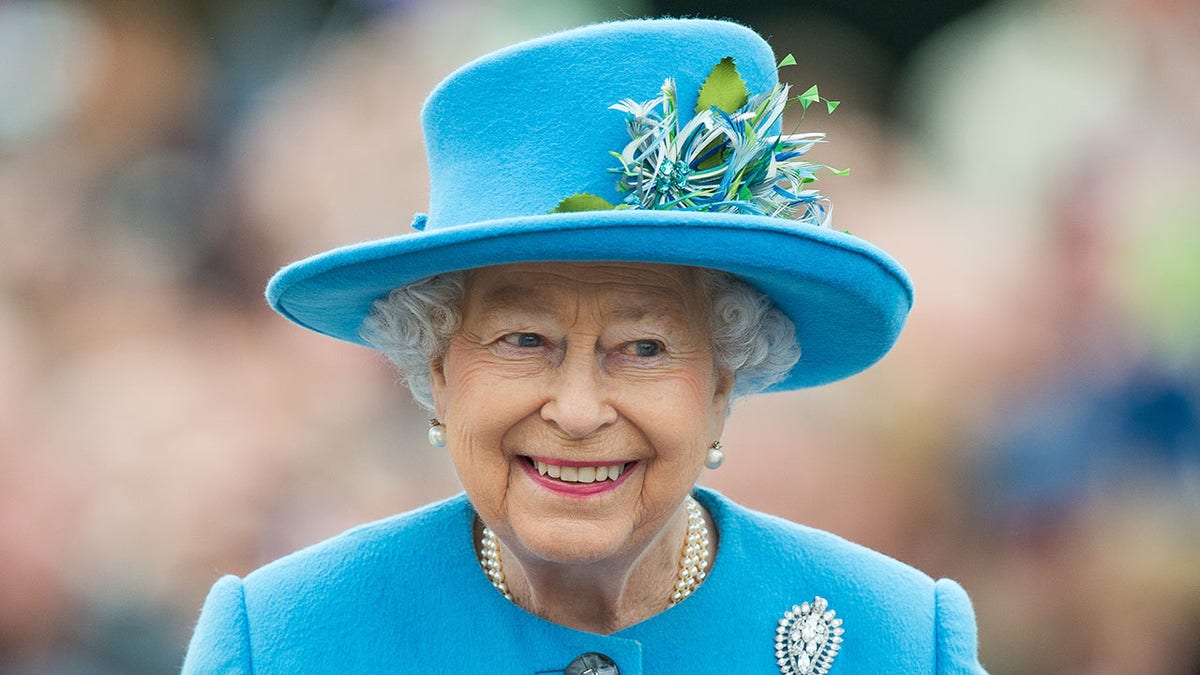 Queen Elizabeth II smiling wearing a blue coat dress and matching hat