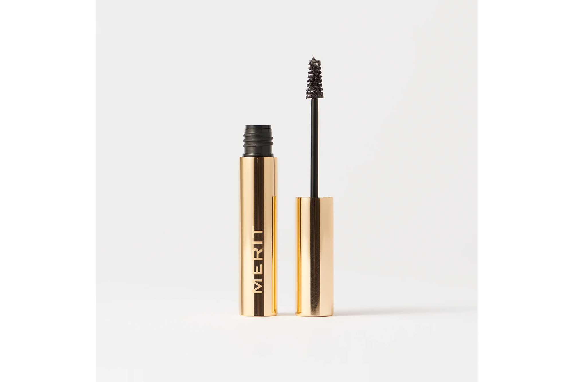 Merit brow gel in a gold tube with the brush extended.