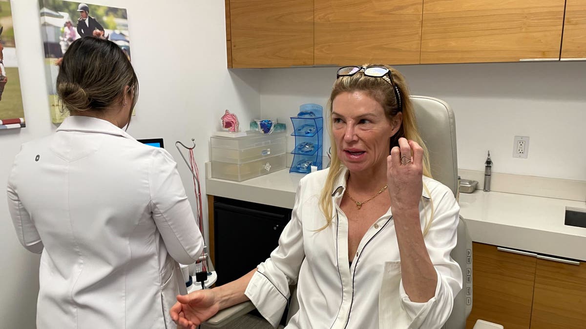 Brandi Glanville sitting in a doctor's office wearing a silk shirt
