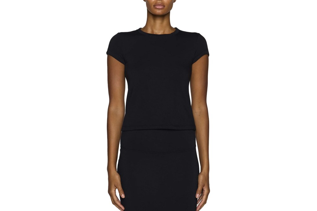 A dark-skinned model wearing a form-fitting black short-sleeved top and a black midi skirt.