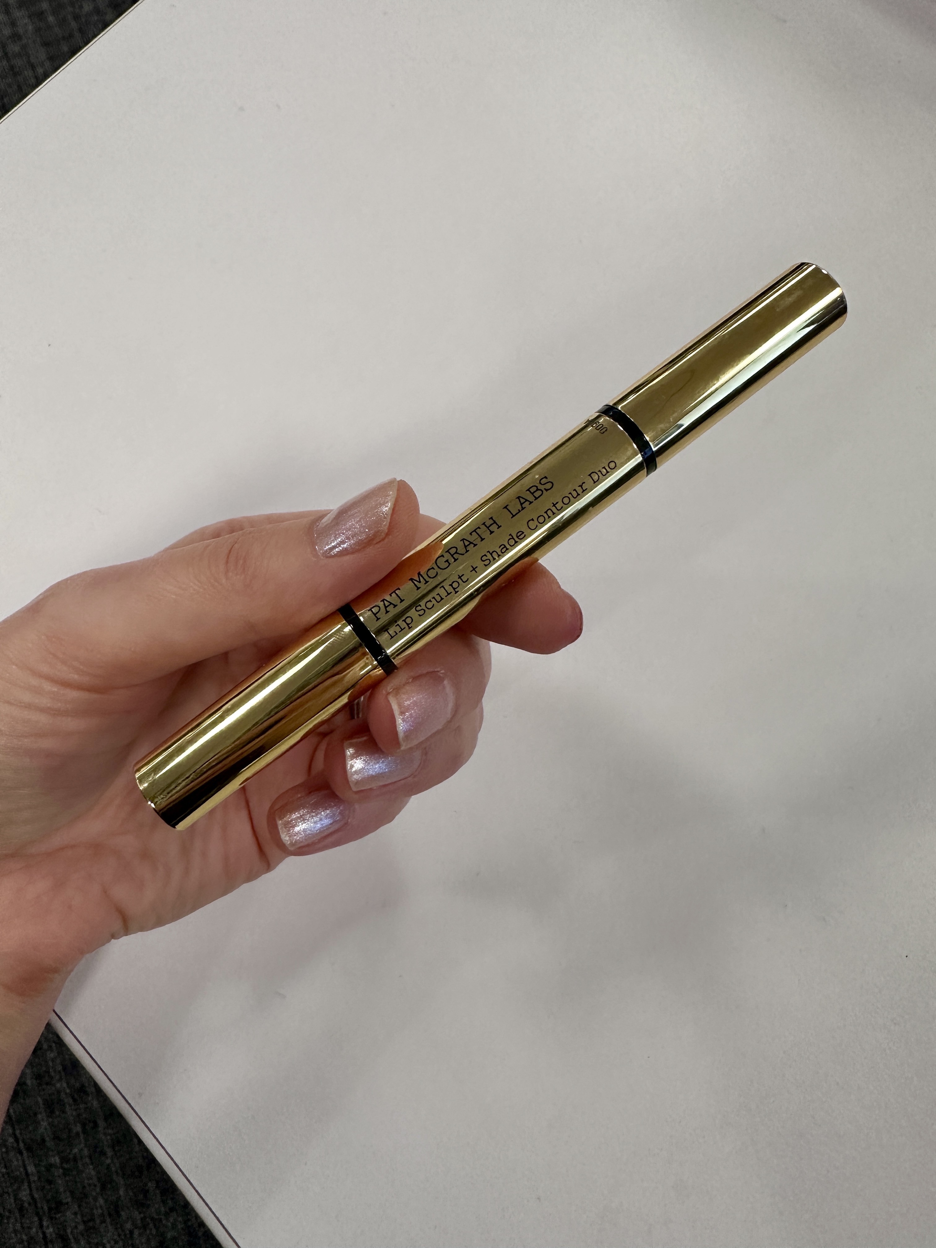 Hand holding a golden Pat McGrath Labs Lip Sculpt and Shade Contour Duo.