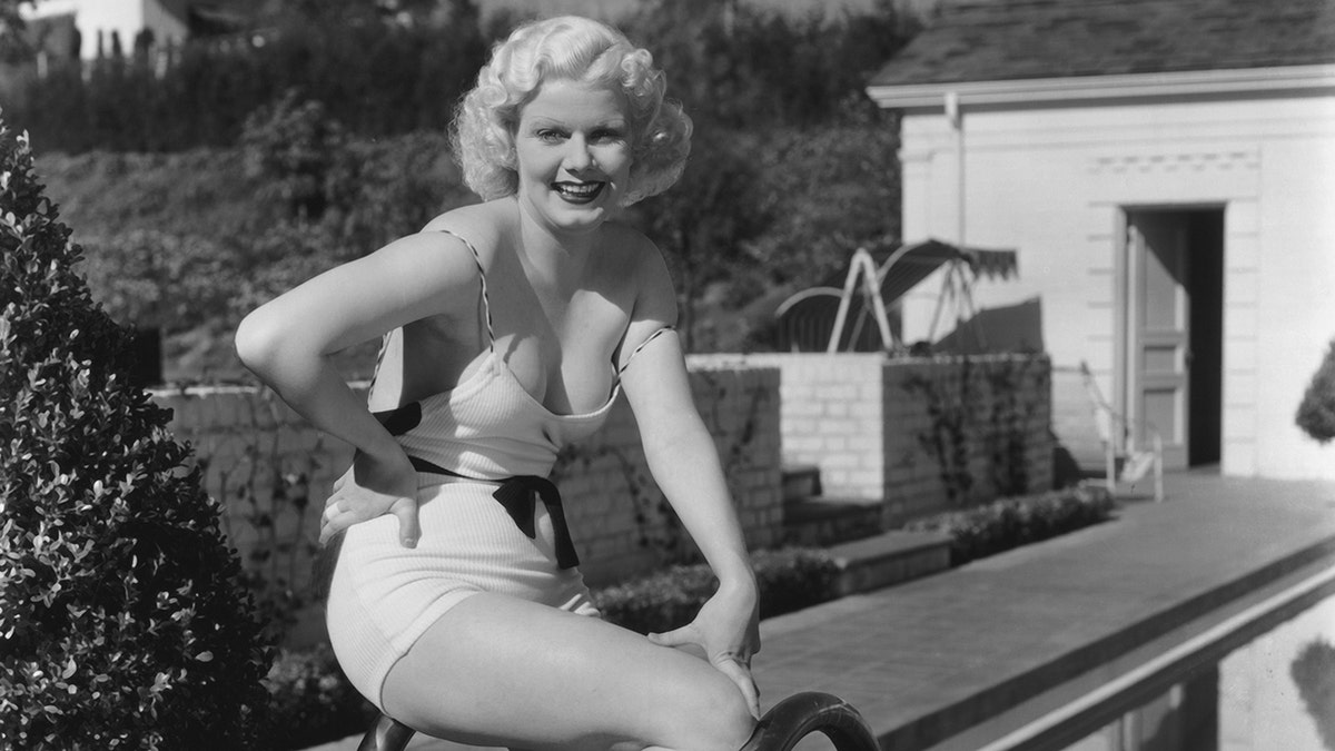 Jean Harlow smiling in her swimsuit while sitting near her pool at her Los Angeles home, in 1933.
