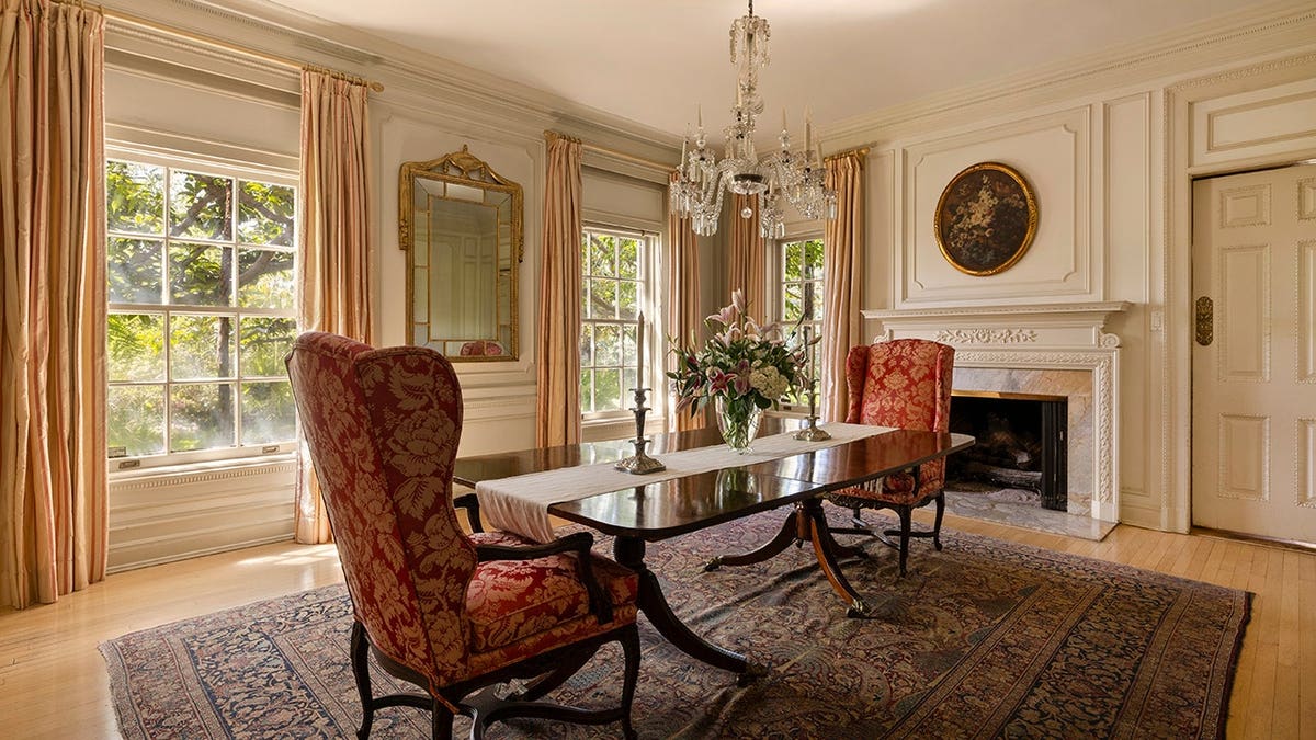 A dining room with two big red chairs around the table and a fireplace.